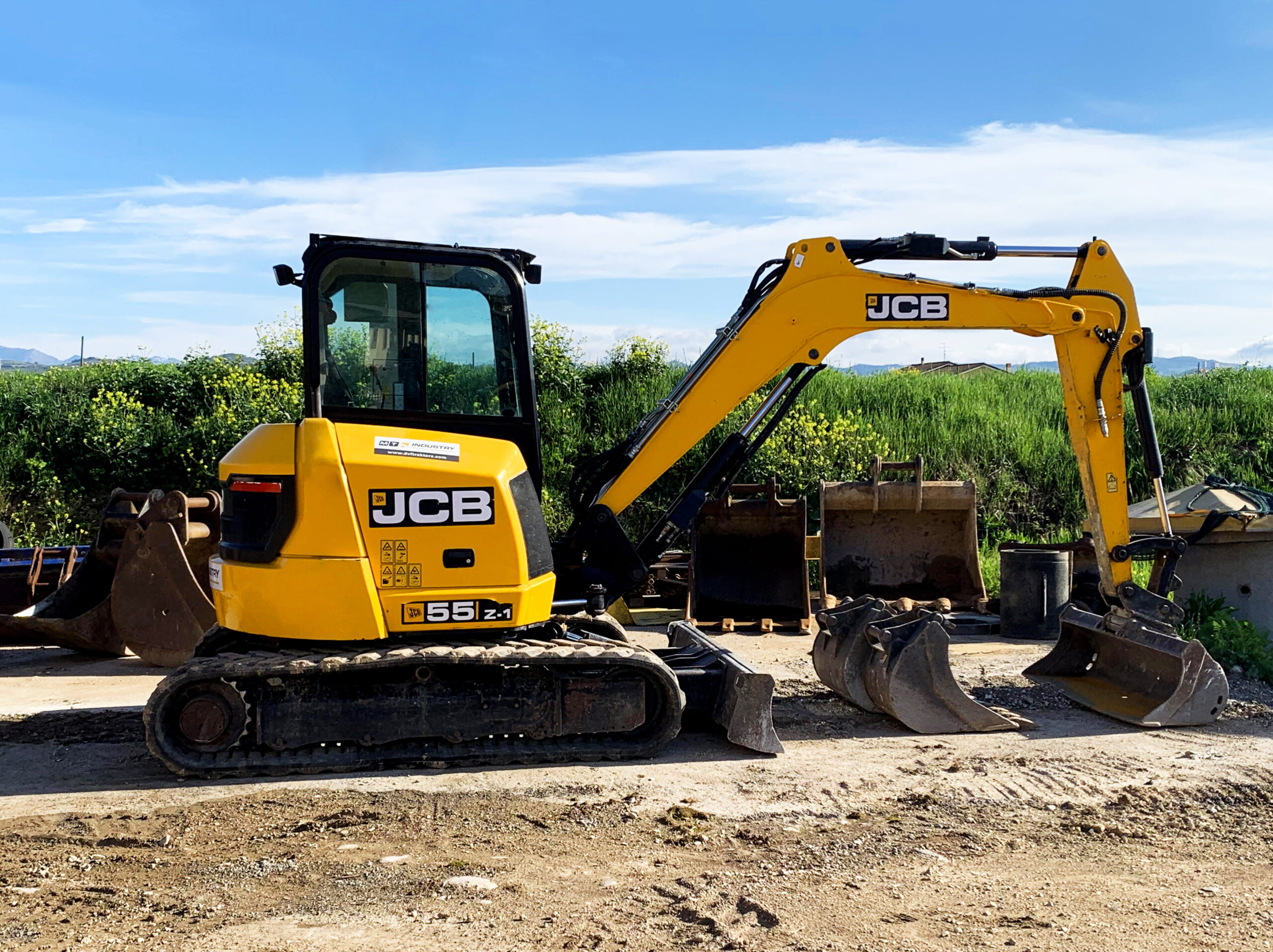 Mini escavatore JCB di colore giallo con dettagli neri su terreno con dietro prato verde e cielo azzurro in una giornata di sole